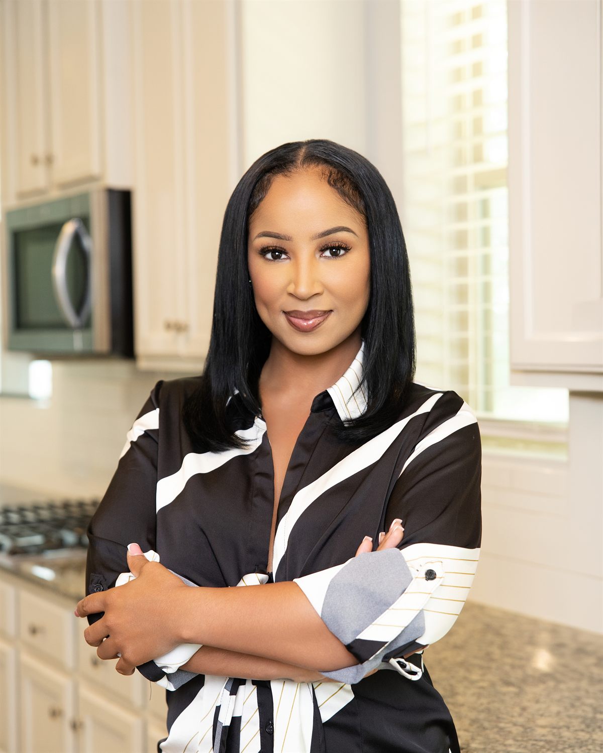 Atlanta realtor smiling with arms crossed in a kitchen, personal branding portrait by ShotByJord